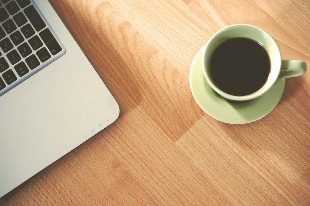 A coffee cup and laptop on a wooden desk, creating a cozy workspace vibe. (Photo by Pixabay on Pexels)