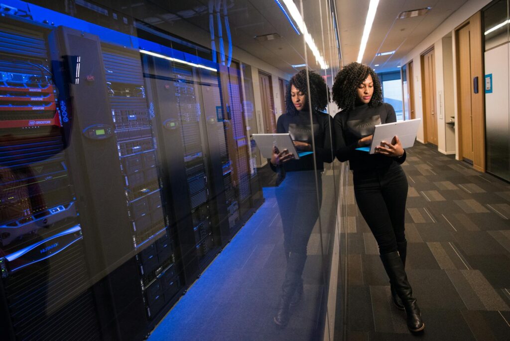 A woman using a laptop navigating a contemporary data center with mirrored servers. (Photo by Christina Morillo on Pexels)