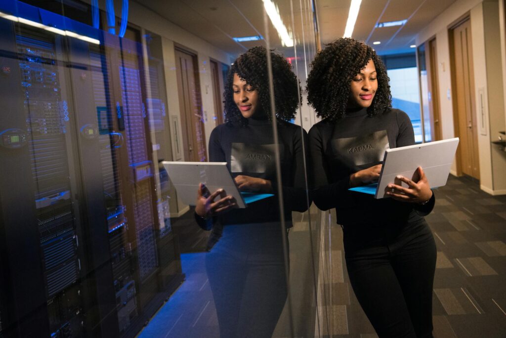 African American woman standing in modern office using laptop, reflecting professionalism and tec... (Photo by Christina Morillo on Pexels)