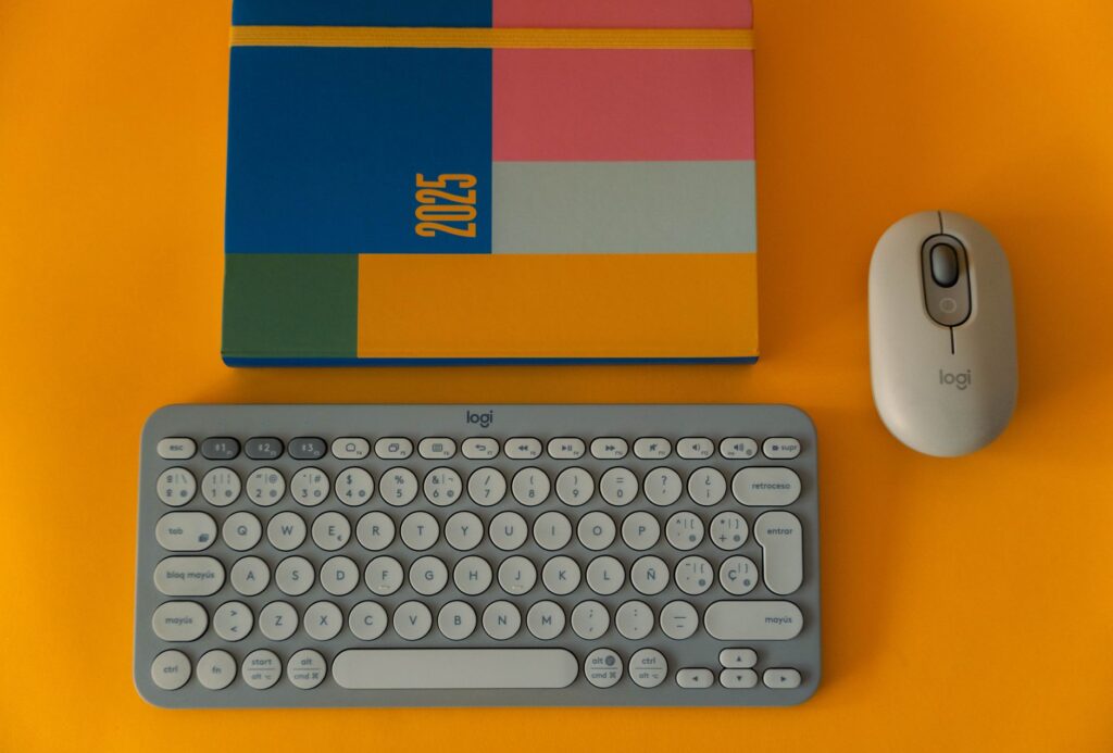 Flat lay of a colorful 2025 planner with keyboard and mouse on a bright orange background. (Photo by Viridiana Rivera on Pexels)
