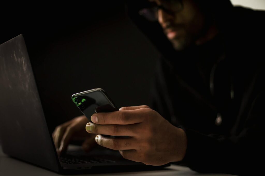 Crop anonymous ethnic male cyber spy with cellphone and netbook hacking system in evening (Photo by Sora Shimazaki on Pexels)