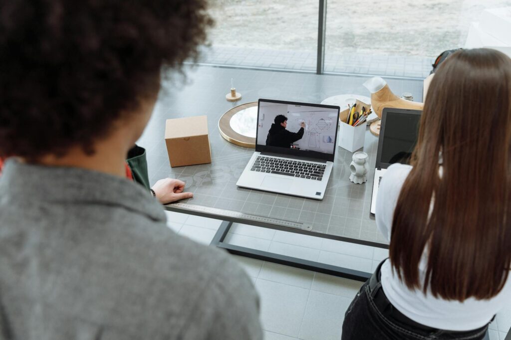 Two colleagues engaging in a remote online meeting at a desk with a laptop. (Photo by Thirdman on Pexels)