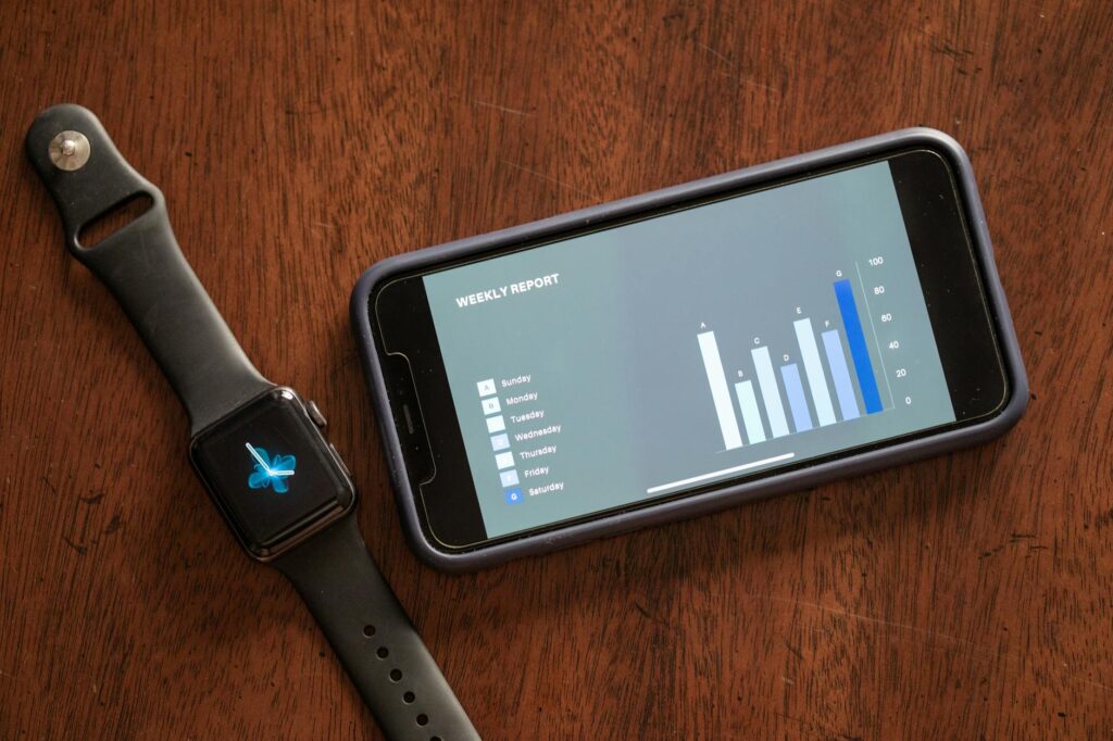 Close-up of a smartphone and smartwatch displaying a weekly report on a wooden table. (Photo by RDNE Stock project on Pexels)