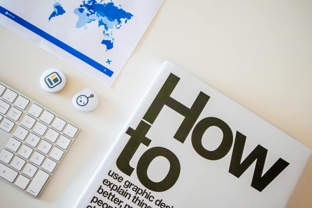 Stylish desk setup with a how-to book, keyboard, and world map on paper. (Photo by Walls.io on Pexels)