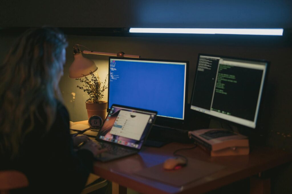 Woman using multiple screens for cybersecurity tasks in a cozy home office (Photo by cottonbro studio on Pexels)