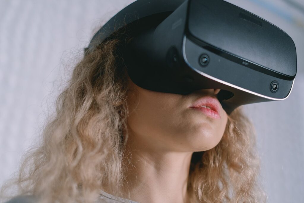 A young woman with curly hair using a VR headset, experiencing virtual reality. (Photo by SHVETS production on Pexels)