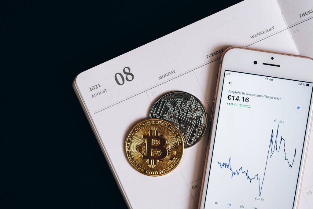 A smartphone displays cryptocurrency data alongside Bitcoin and Ethereum coins on an August calen... (Photo by Leeloo The First on Pexels)