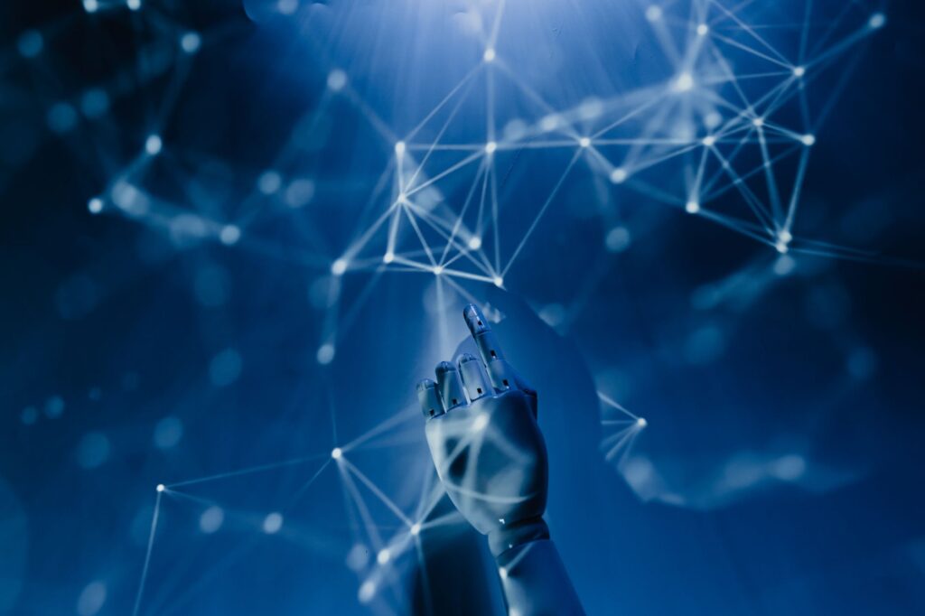 A robotic hand reaching into a digital network on a blue background, symbolizing AI technology. (Photo by Tara Winstead on Pexels)