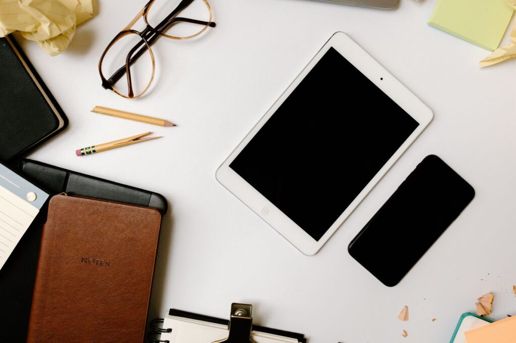 Top view of a desk with gadgets, glasses, and notebooks in an organized arrangement. (Photo by Tara Winstead on Pexels)