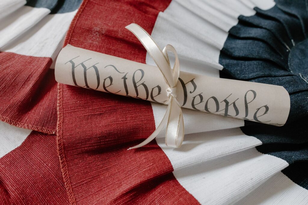 Close-up of a 'We the People' scroll on an American flag cloth background. (Photo by Tara Winstead on Pexels)